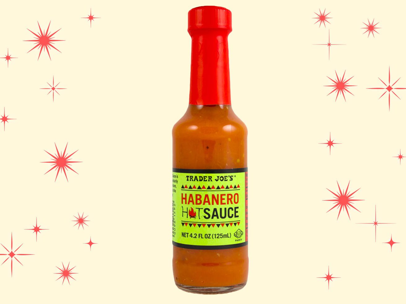 A bottle of Trader Joe’s habanero hot sauce with a fluorescent green label and a red cap floating on an illustrated salmon-colored background with red, mid-century star bursts.