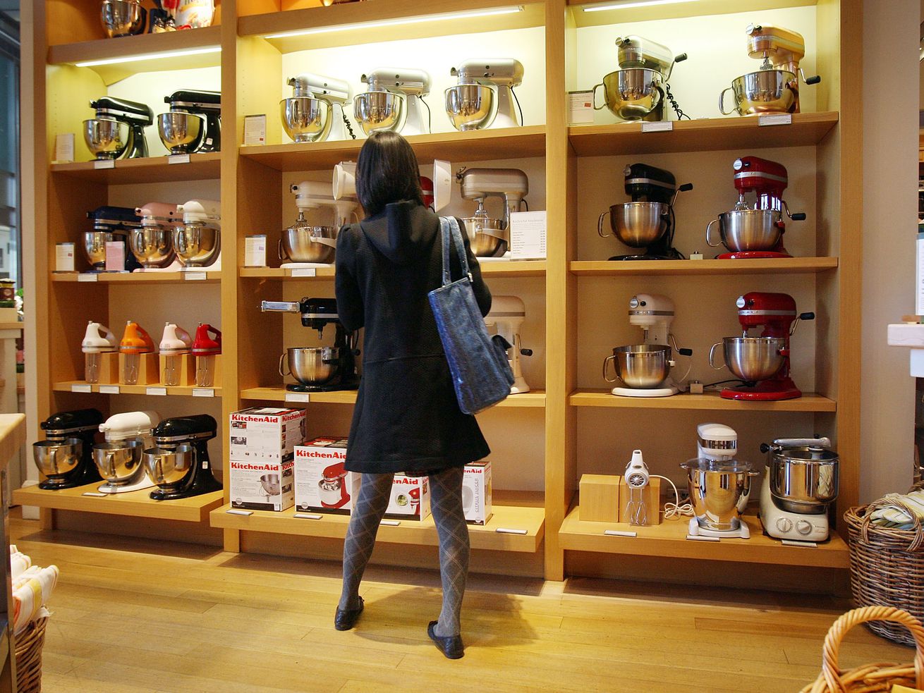 A woman stands with her back to camera looking up at shelf of KitchenAid stand mixers at a Williams-Sonoma store