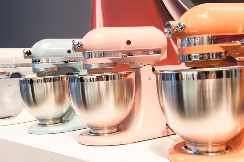 Four KitchenAid stand mixers on display, one white, one pale blue, one pale pink, and one pale orange